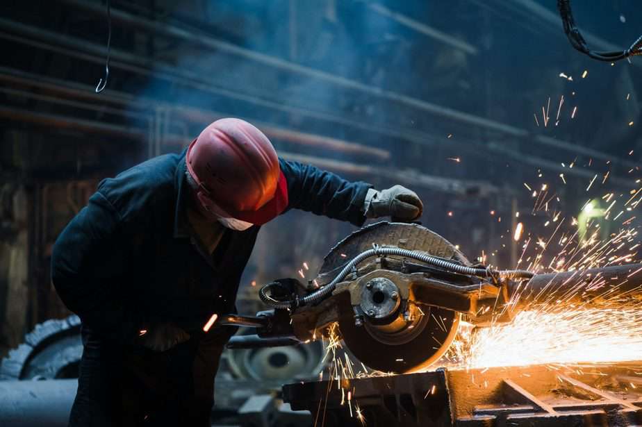 Employee grinding steel with sparks - focus on grinder. Steel factory